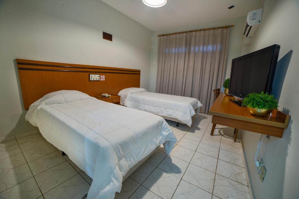 a hotel room with two beds and a flat screen tv at Hotel Leiria in Matão
