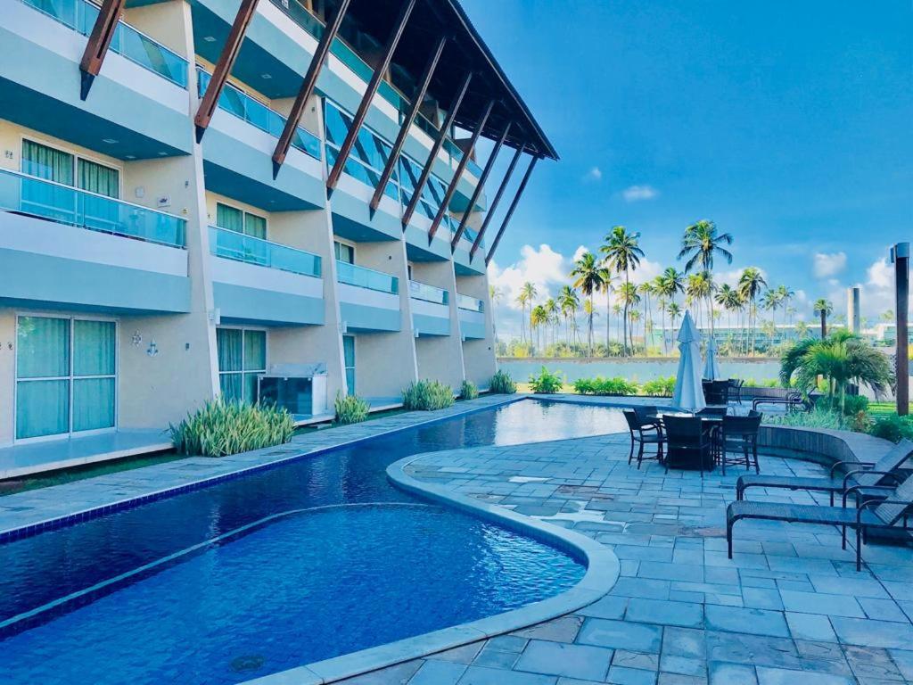 a resort swimming pool with tables and chairs next to a building at Condomínio Villas do Atlântico in Porto De Galinhas