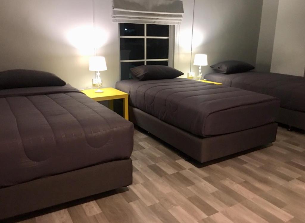 A three-bed room with dark bedding, bedside lamps, and a curtained window.