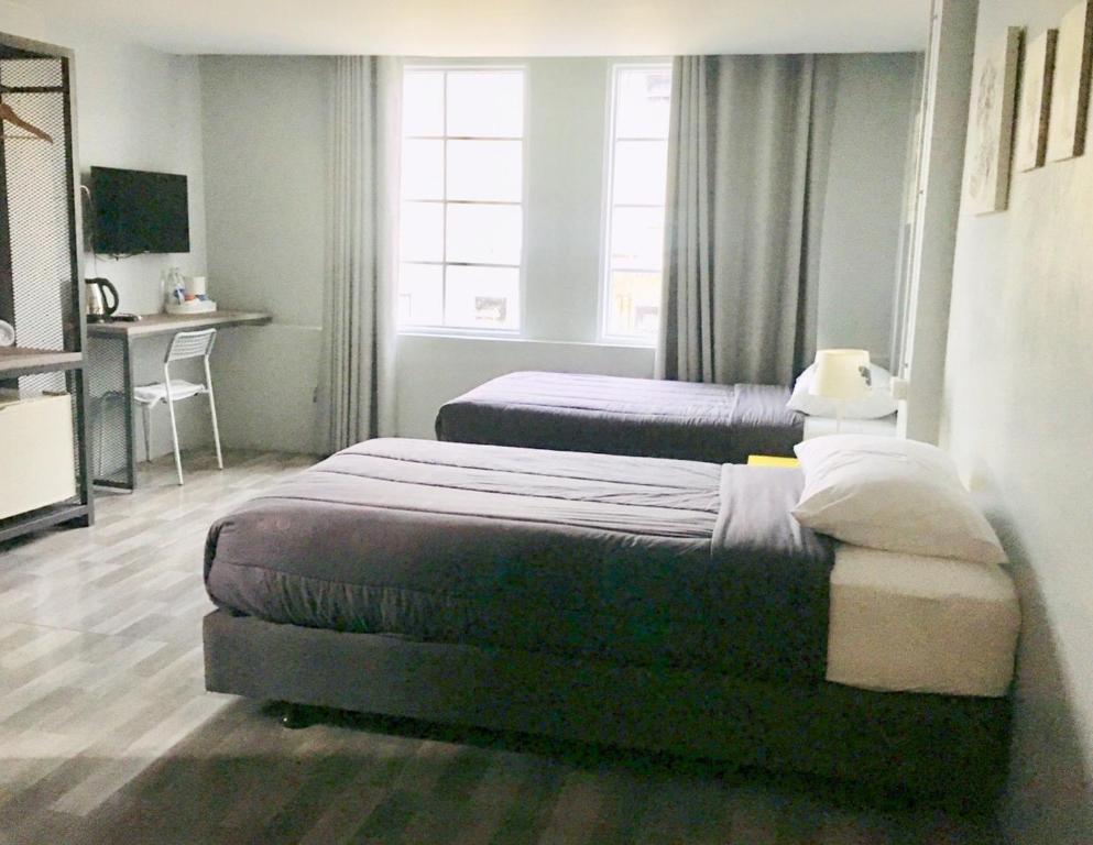 A bright twin room with a desk, TV, tea setup, and two windows.