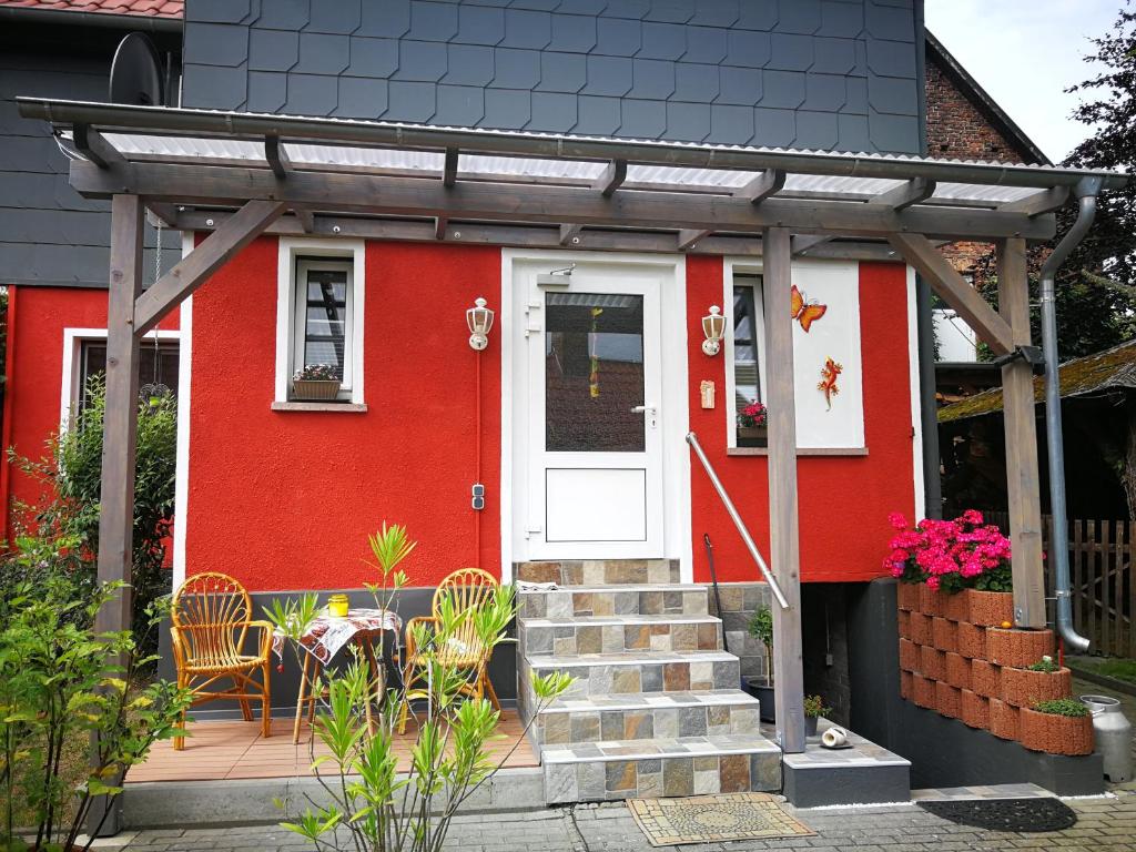 ein rotes Haus mit einer weißen Tür sowie einem Tisch und Stühlen in der Unterkunft Ferienwohnung am Finkenherd in Dankerode