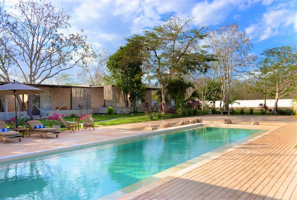 a swimming pool in a yard with chairs and an umbrella at Hotel Casa de Campo Conkal Merida in Conkal