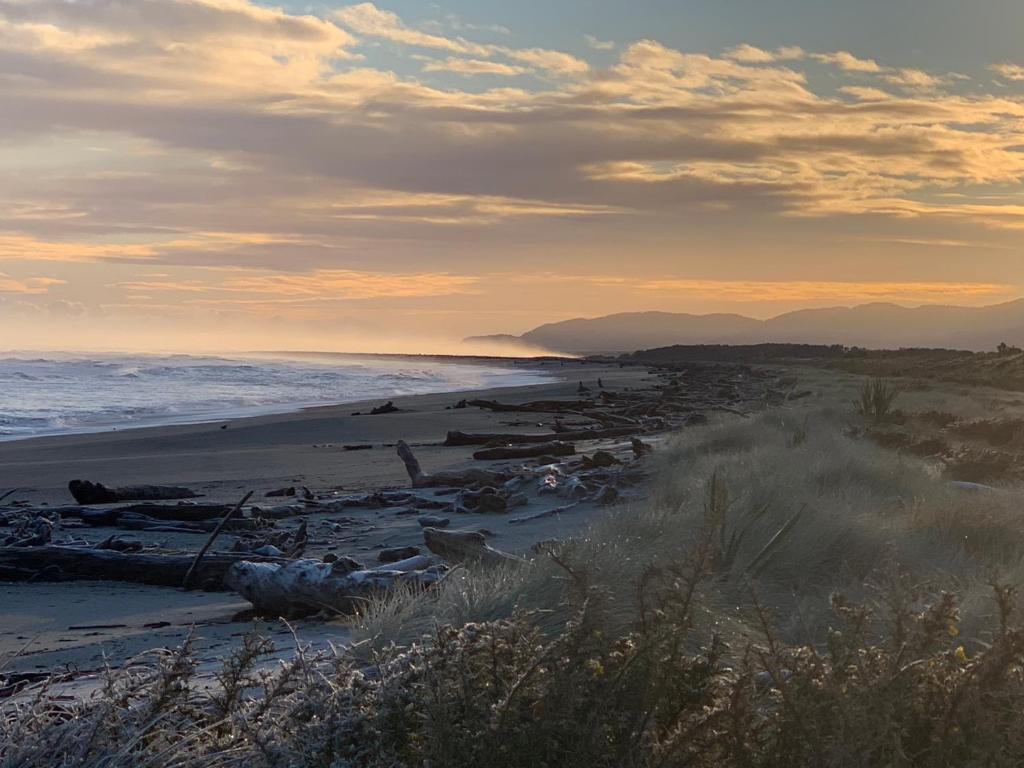 een strand bij zonsondergang met de oceaan en de bergen bij Haast Beach Motel in Haast