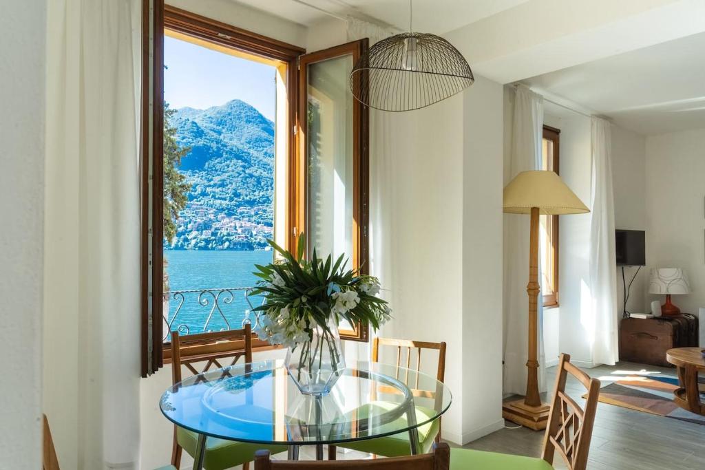 una sala da pranzo con tavolo in vetro e ampia finestra di Romantic Pier by Rent All Como a Carate Urio