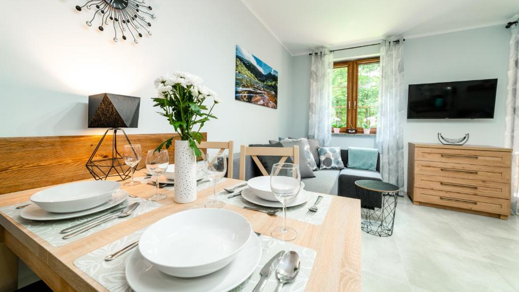 uma sala de estar com uma mesa com pratos brancos em Apartamenty EverySky - Leśny Dom 16 - 18 em Karpacz