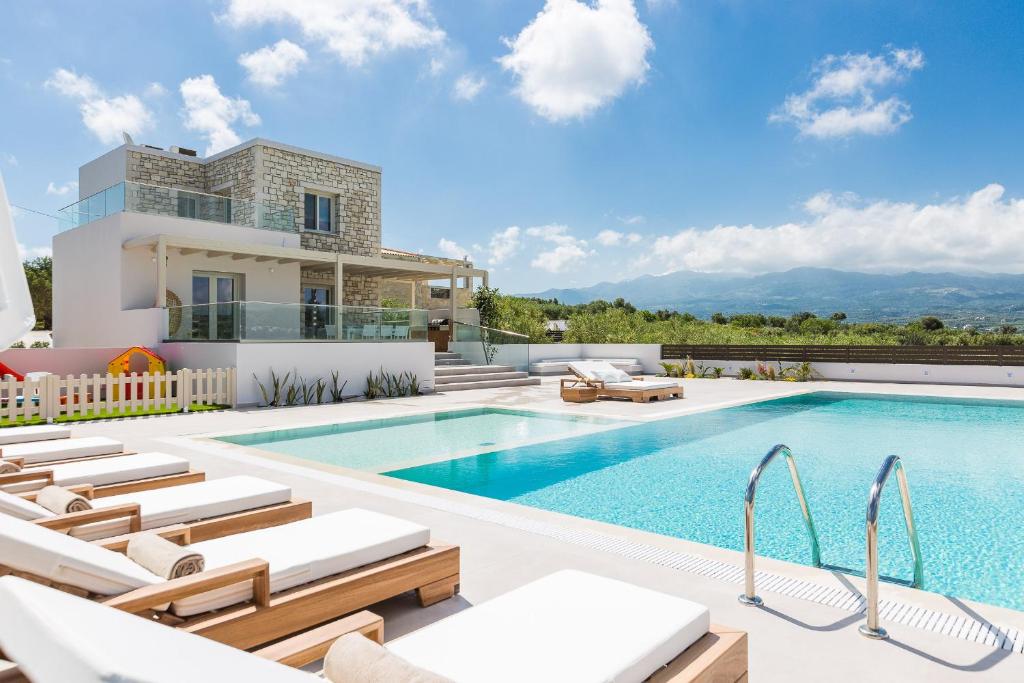 a villa with a swimming pool and lounge chairs at Rosmerta Villa, Chic & Prestigious, By ThinkVilla in Perama