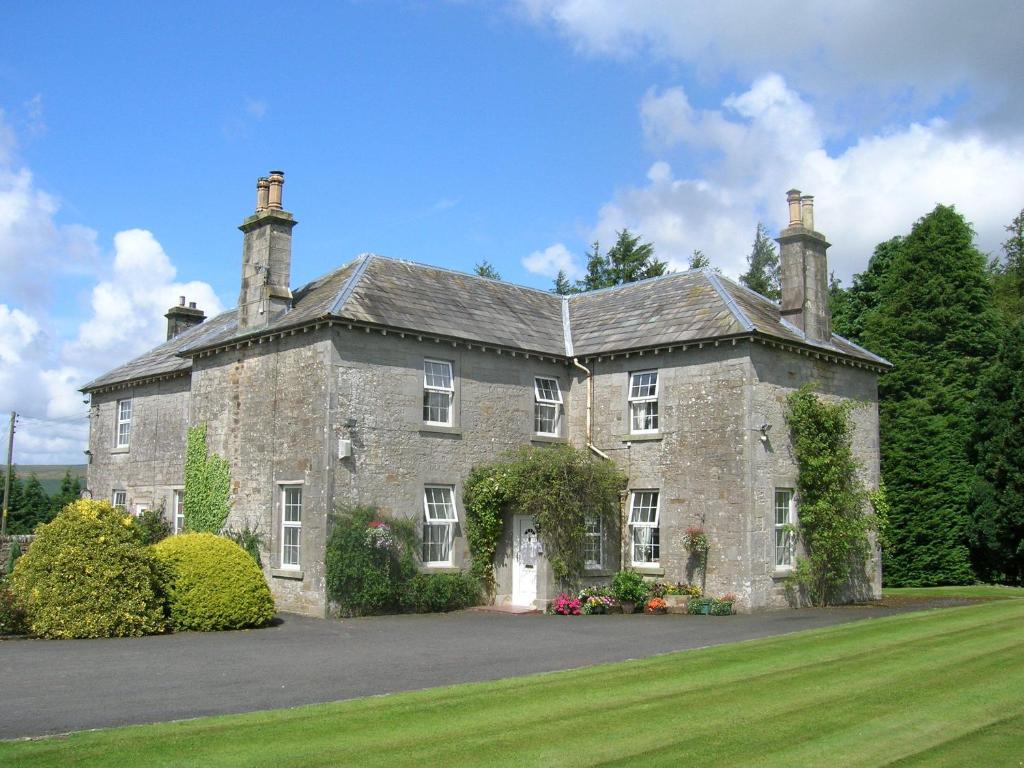a large stone house with a grass yard at Sorbietrees B&B in Newcastleton