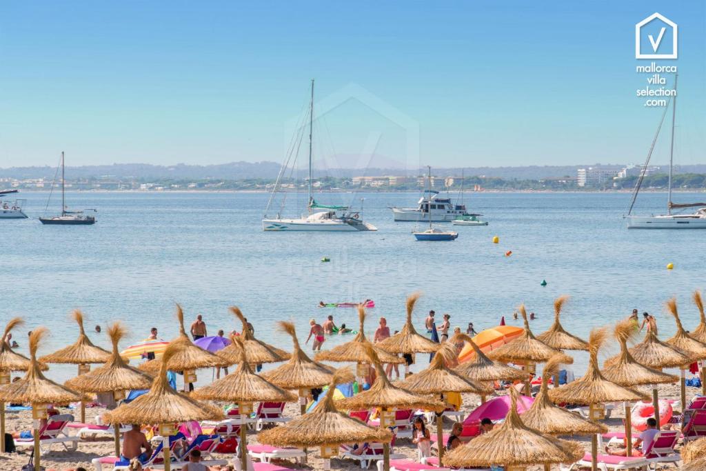 eine Gruppe von Menschen am Strand mit Sonnenschirmen und Booten in der Unterkunft Apartamentos DIANA Alcudia in Alcúdia