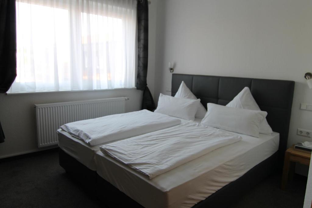 Una cama con sábanas blancas y almohadas en un dormitorio en Hotel & Restaurant Blume en Wolfsburg