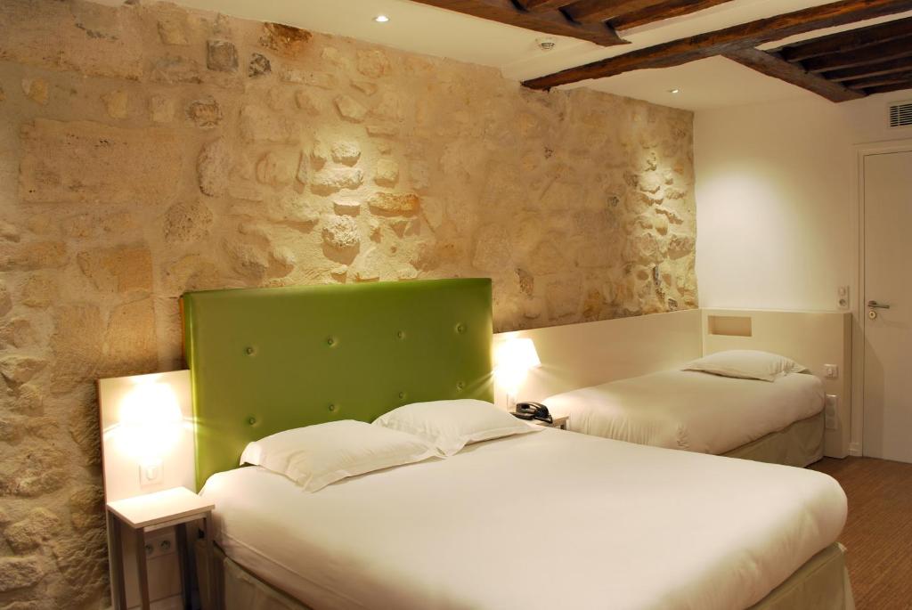 two beds in a room with a stone wall at Hôtel De La Herse d'Or in Paris