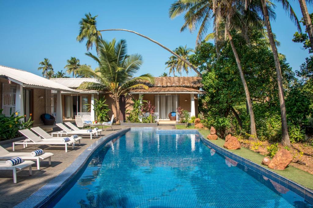 a swimming pool in front of a house with palm trees at Casa Vagator in Vagator