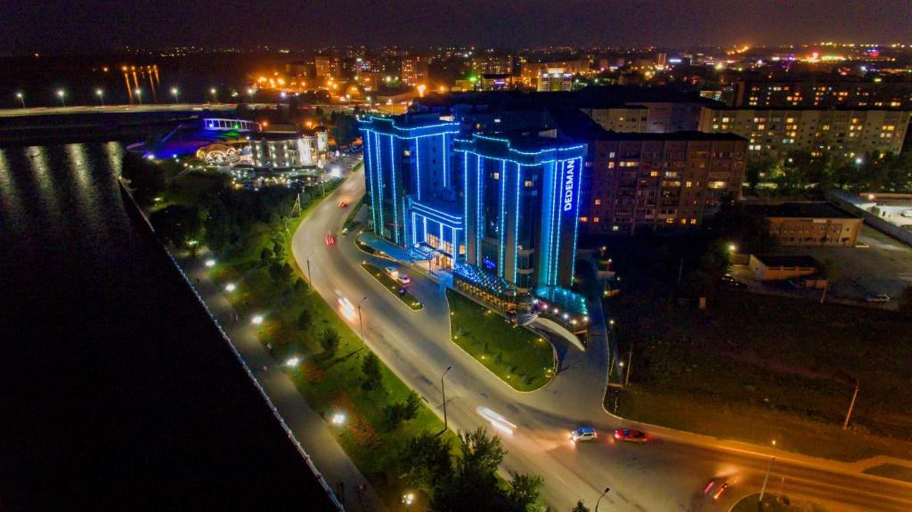 a city at night with a blue building with lights at Dedeman Oskemen Tavros Hotel in Ustʼ-Kamenogorsk