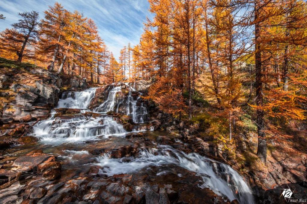 una cascada en el bosque con árboles de otoño en APPARTEMENT 4 PERSONNES A 500M DES TELECABINES, en Briançon