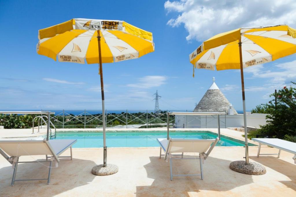 una piscina con 2 sombrillas amarillas y blancas en HelloAPULIA - Panoramic Trullo Blue Ocean View, en Monopoli