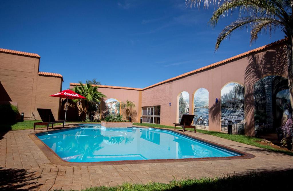 einen Pool mit 2 Stühlen und einem Sonnenschirm in der Unterkunft Desert Palace Hotel in Upington