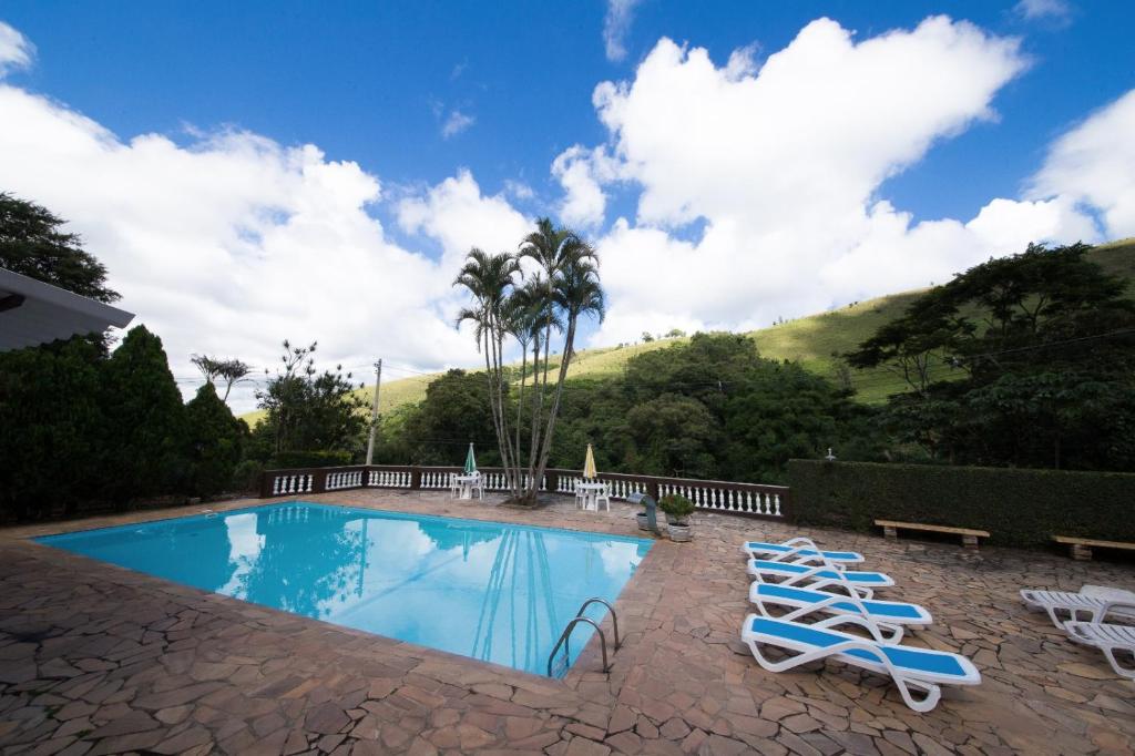 a swimming pool with two lounge chairs and palm trees at Pousada Ypê das Montanhas in Monte Alegre do Sul