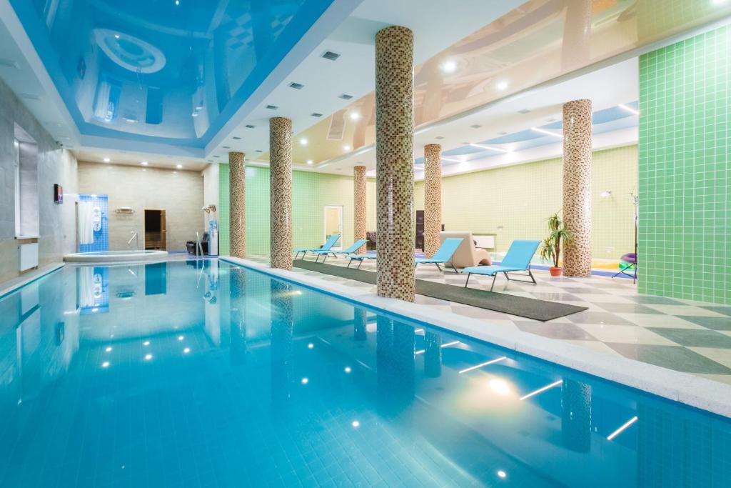 a swimming pool in a hotel lobby with blue chairs at Triumph Hotel in Krasnodar