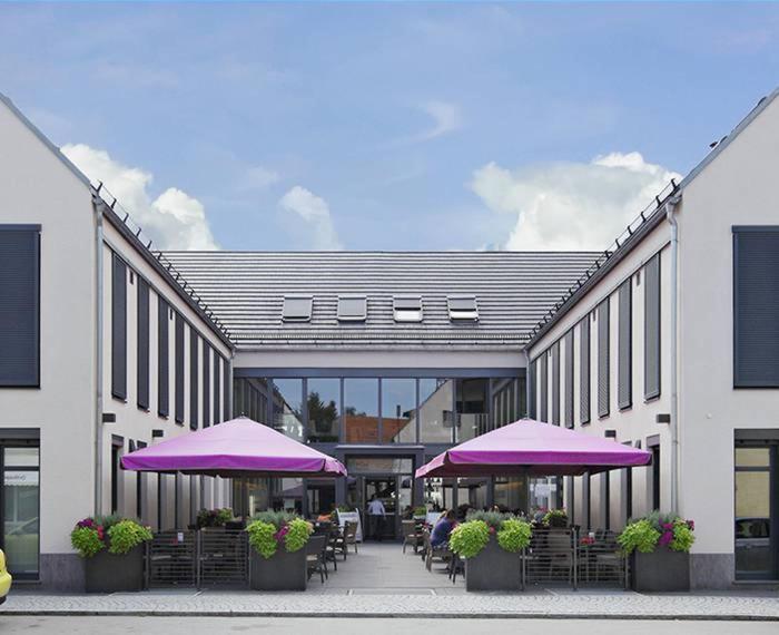 a building with purple umbrellas and tables and chairs at KH Hotel mit Restaurant in Geisenfeld