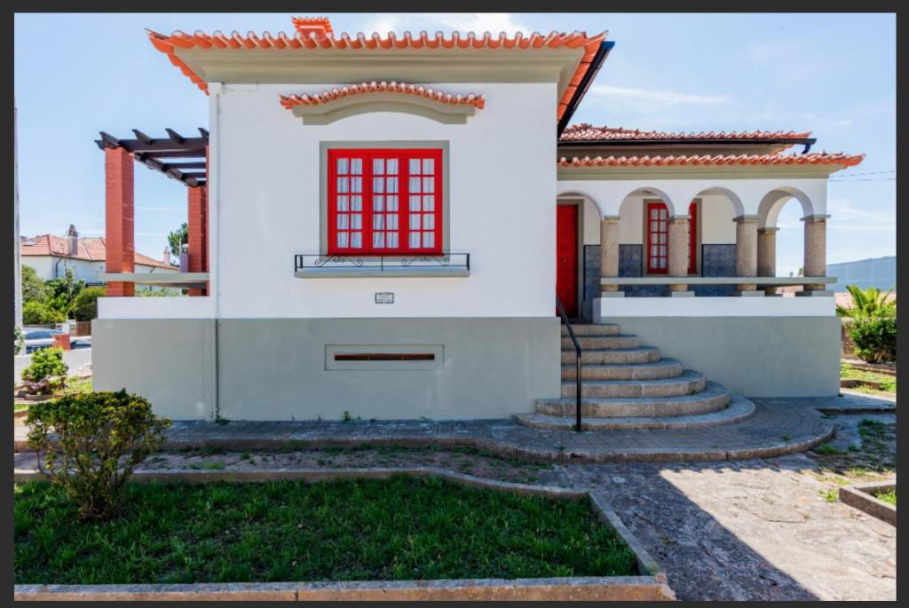 a small white house with red windows and stairs at Beach Park Guesthouse in Vila do Conde