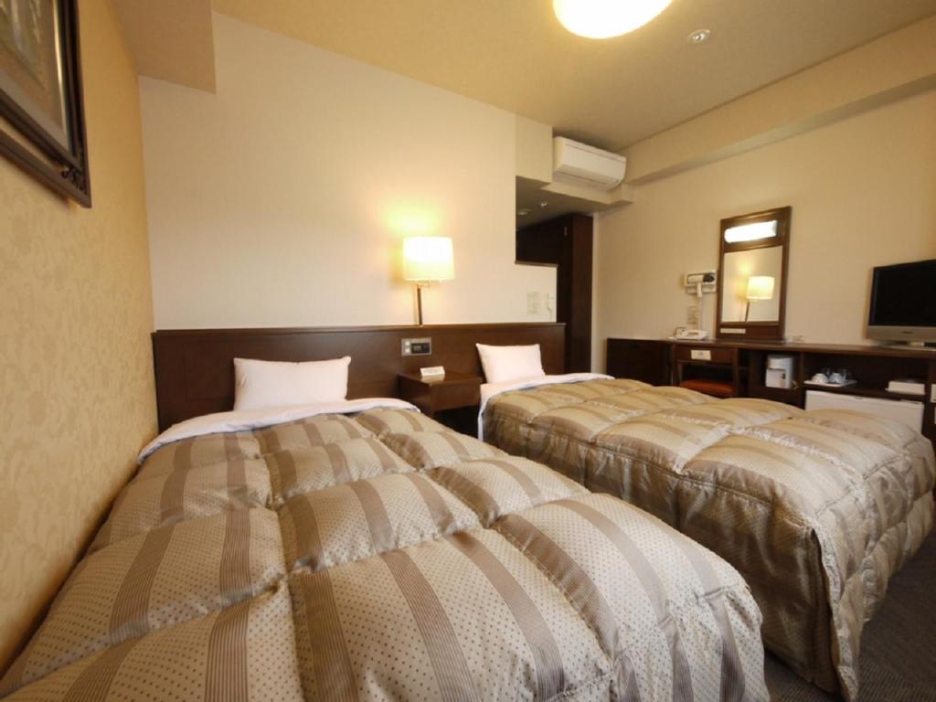 a hotel room with two beds and a television at Hotel Route-Inn Suwa-Inter2 in Suwa