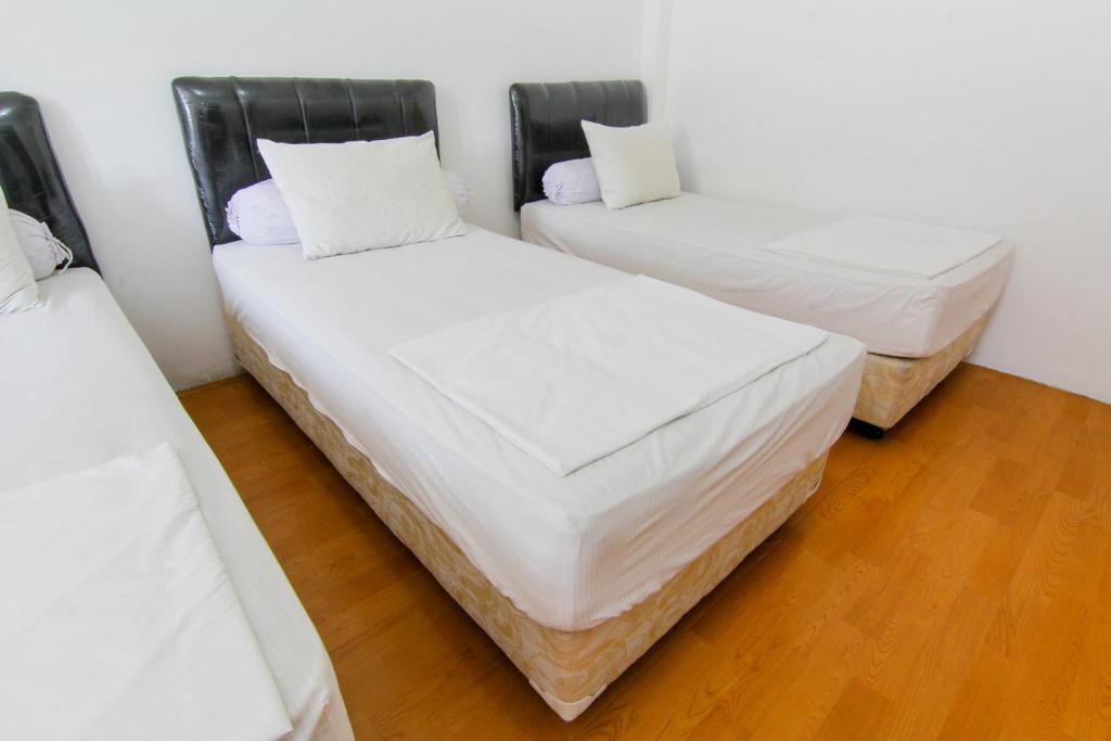 two beds in a room with white sheets and pillows at Lestari Guesthouse in Padang