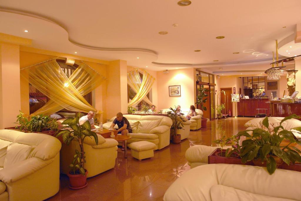 a lobby with white couches and plants and people at Elegant Hotel in Bansko