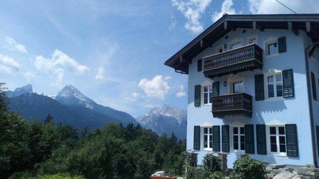 a white building with balconies and mountains in the background at Die schlafende Goass - Pub und Gästehaus in Bischofswiesen