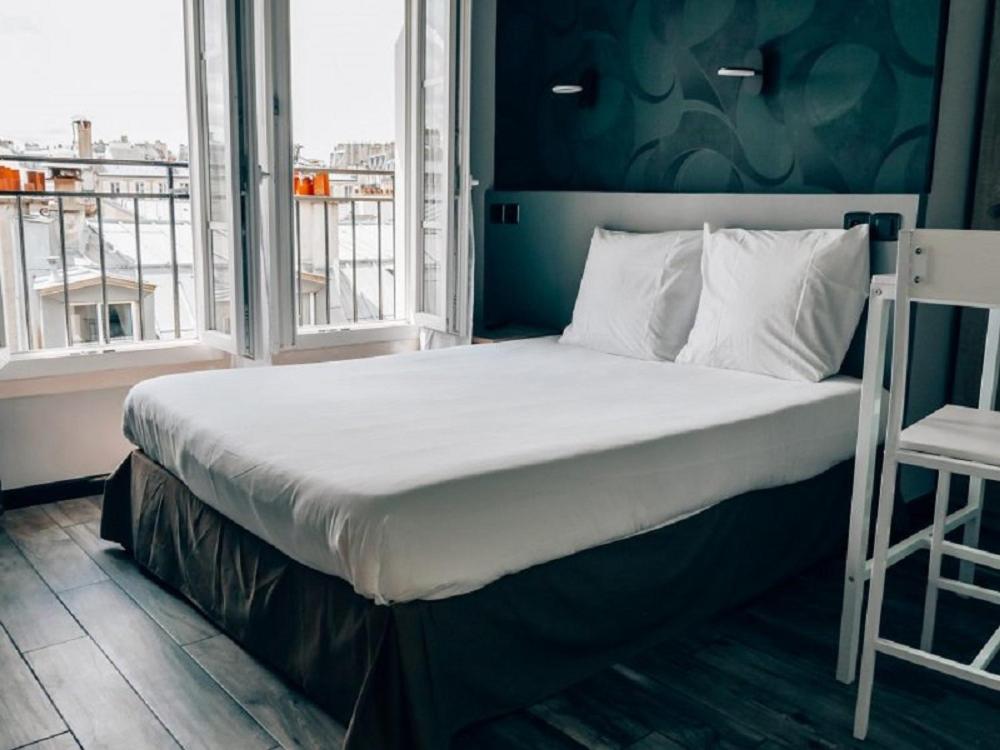 een groot bed in een kamer met een raam bij Hotel Luxia in Parijs