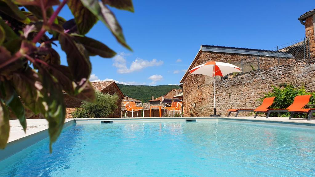 a swimming pool with orange chairs and an umbrella at Chambres d'hôtes Vers la Croix in Leynes