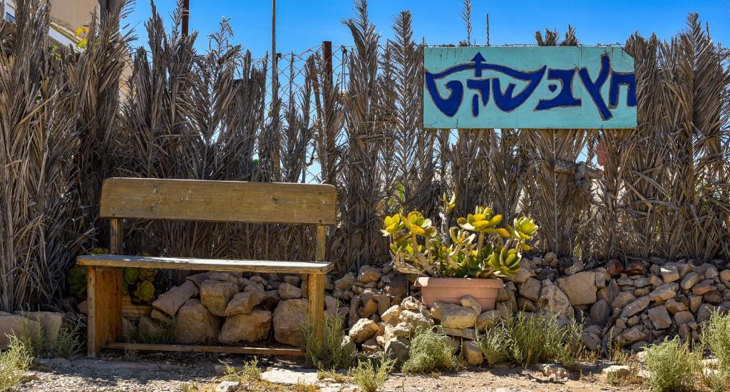 a bench sitting next to a pile of rocks and flowers at Silent Arrow in Mitzpe Ramon