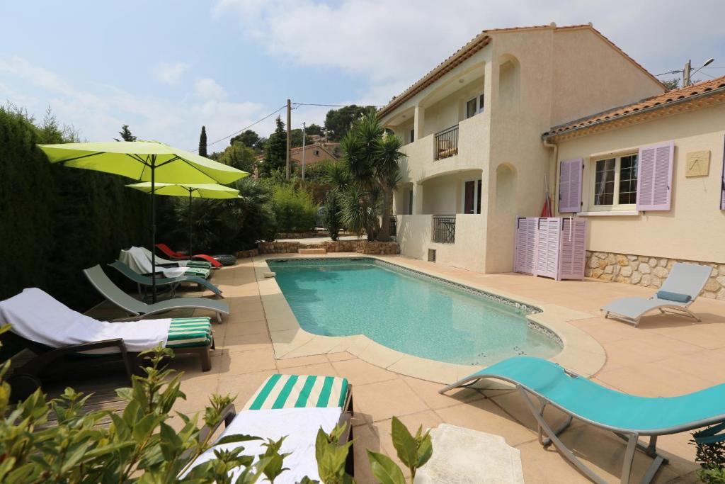 einen Pool mit Stühlen und einem Sonnenschirm neben einem Haus in der Unterkunft La Bastide des Pins in Le Pradet