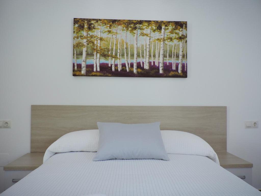Un dormitorio con una cama blanca con un cuadro encima. en Hostal Delia en Alora