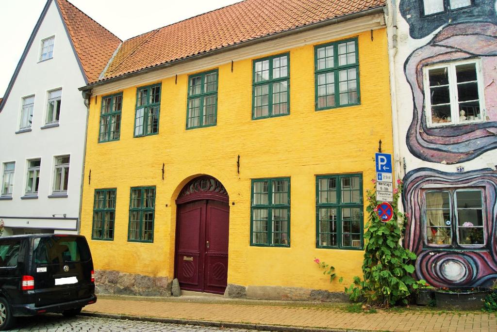 um edifício amarelo com uma porta vermelha numa rua em Das Gelbe Haus - Drei besondere Ferienwohnungen em Flensburg