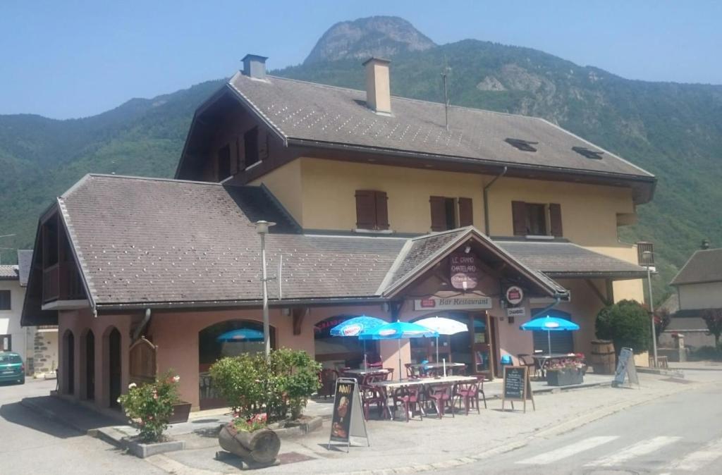 een groot gebouw met tafels en blauwe parasols bij Le Grand Chatelard HÔTEL BAR RESTAURANT in Sainte-Marie-de-Cuines