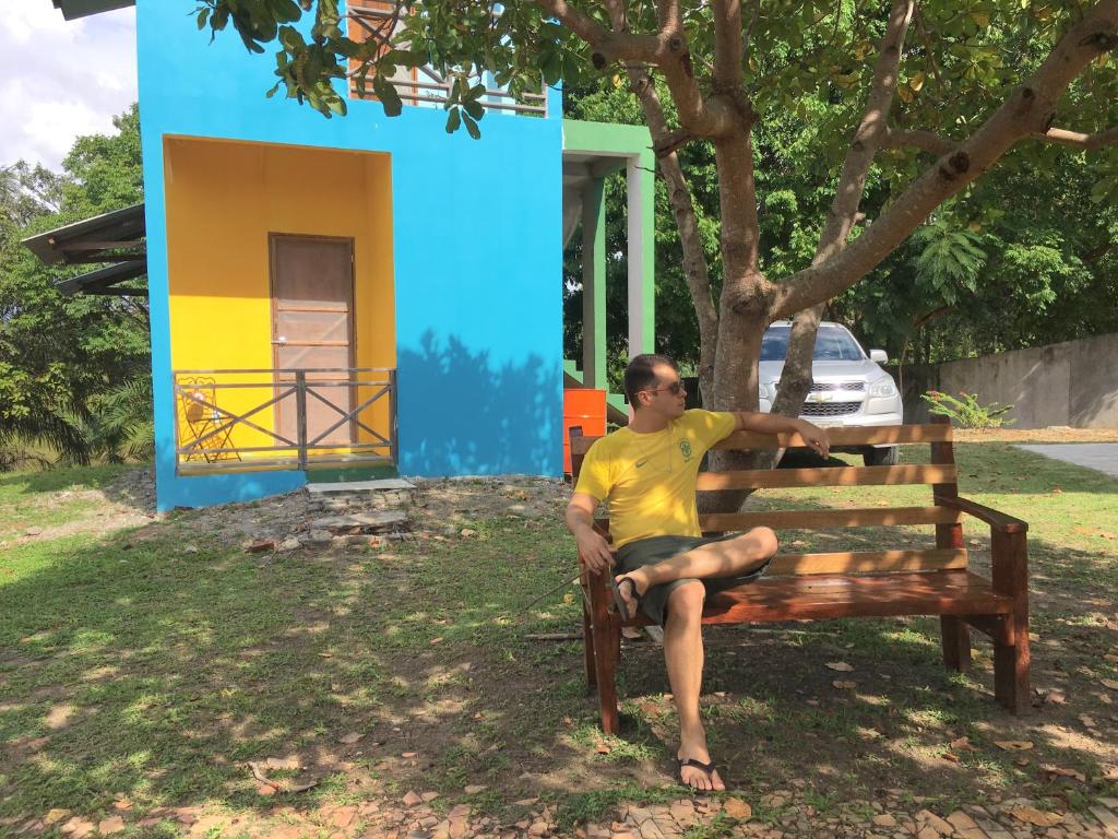 a man sitting on a bench under a tree at Chalé Quintal Amazon in Macapá