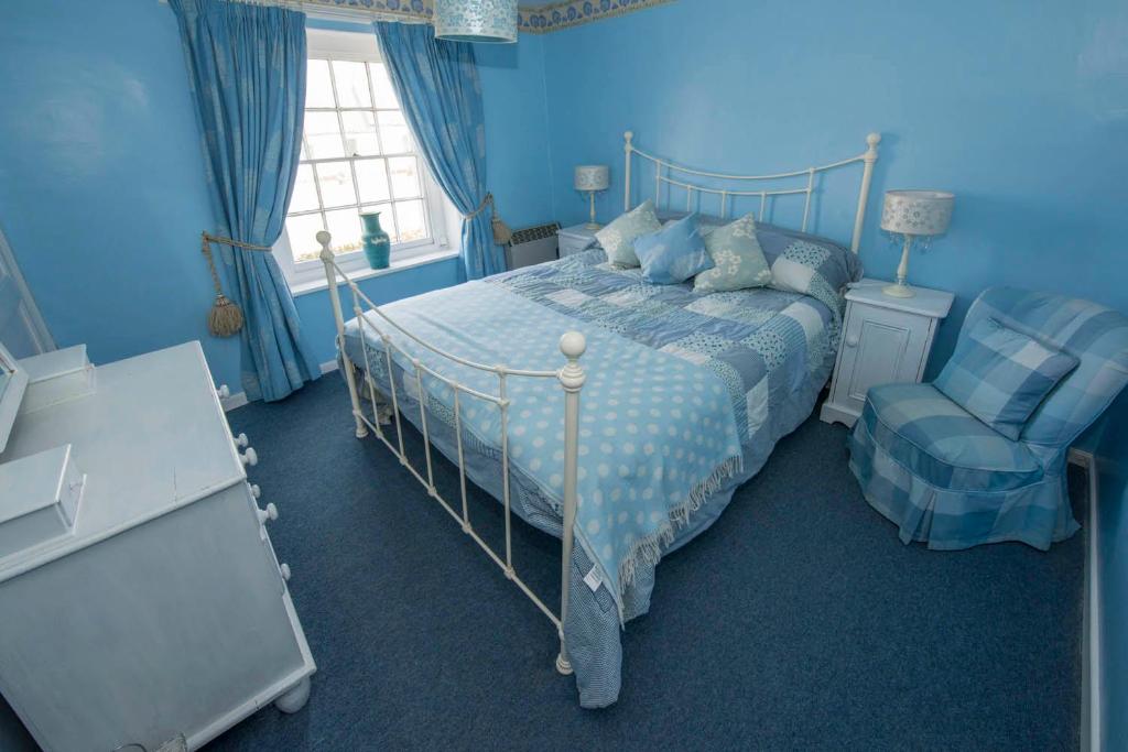 a blue bedroom with a bed and a chair at Delphinium Cottage in Holt