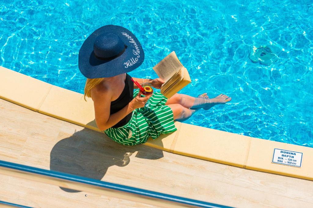 a woman in a hat reading a book next to a swimming pool at Villa Sunce in Orasac