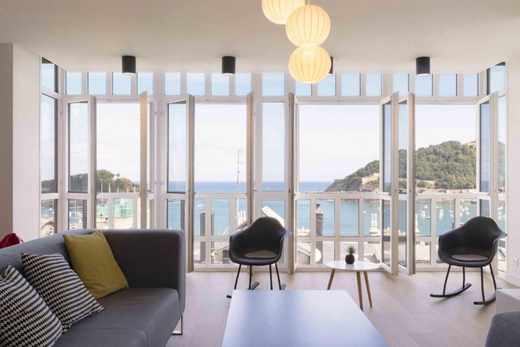 a living room with a couch and chairs and large windows at The Rentals Collection - Treasure in San Sebastián