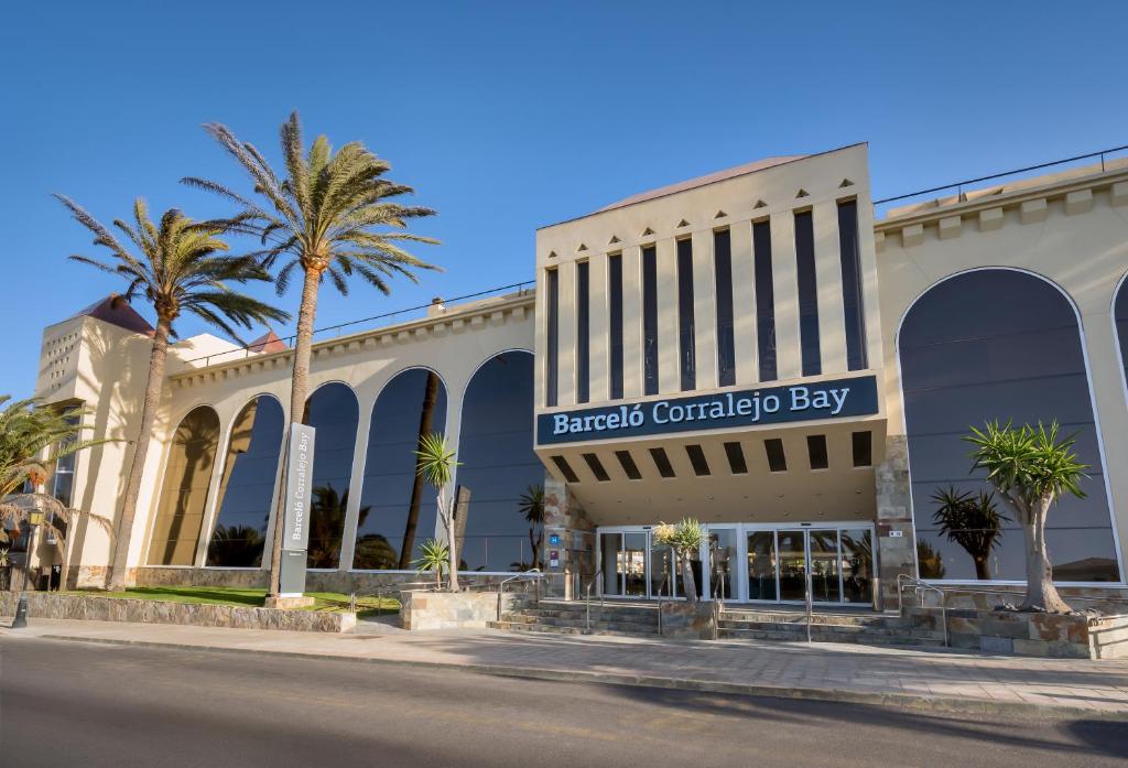 a shopping center with palm trees in front of a building at Barceló Corralejo Bay - Adults Only in Corralejo