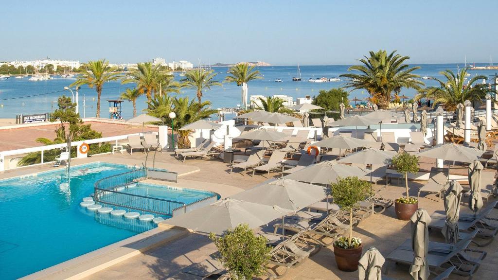 a resort with a swimming pool and chairs and the ocean at Bellamar Hotel Beach & Spa in San Antonio