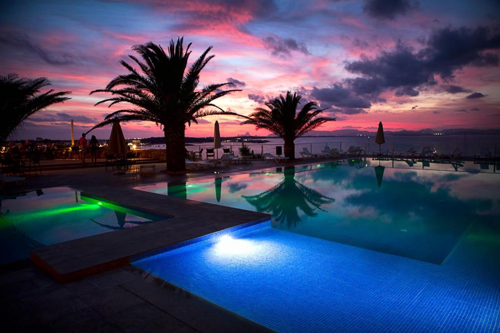 uma piscina com palmeiras e um pôr-do-sol em Hotel Club Sunway Punta Prima em Es Pujols