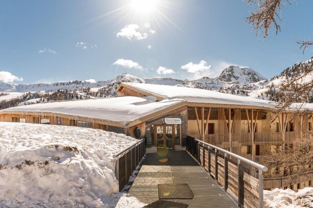a building covered in snow with mountains in the background at Residence Les Terrasses d'Azur - maeva Home in Isola 2000