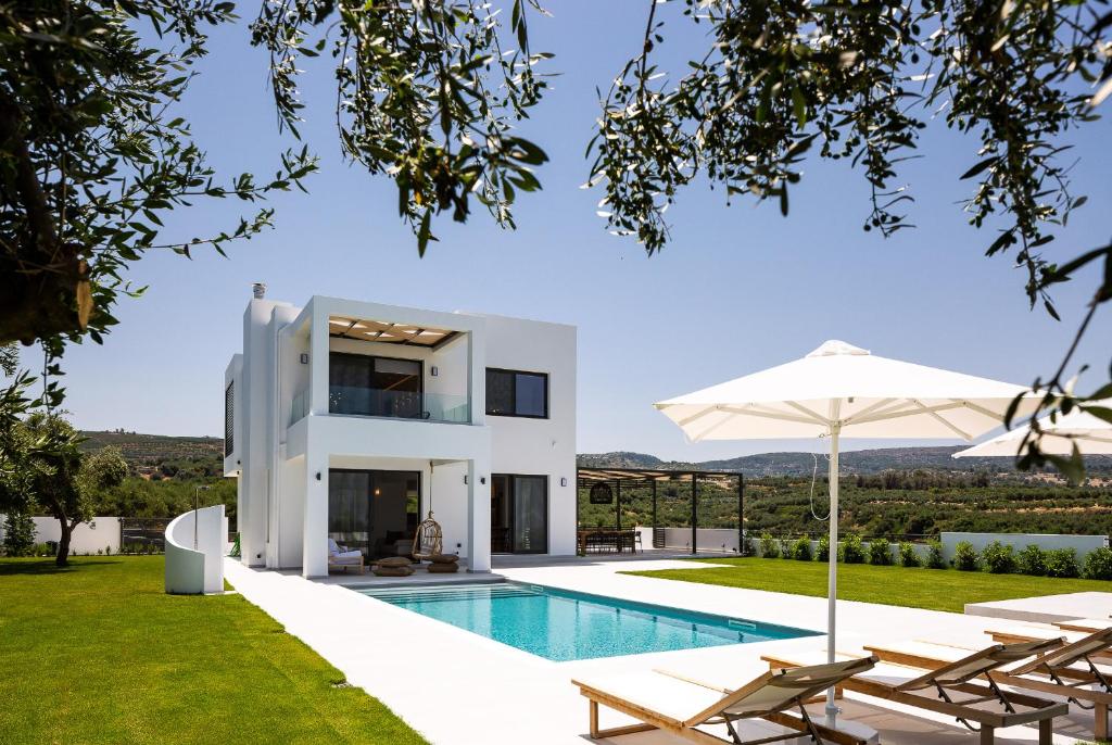 a white villa with a swimming pool and lawn at Vilana White Elegant Villa in Roúpai