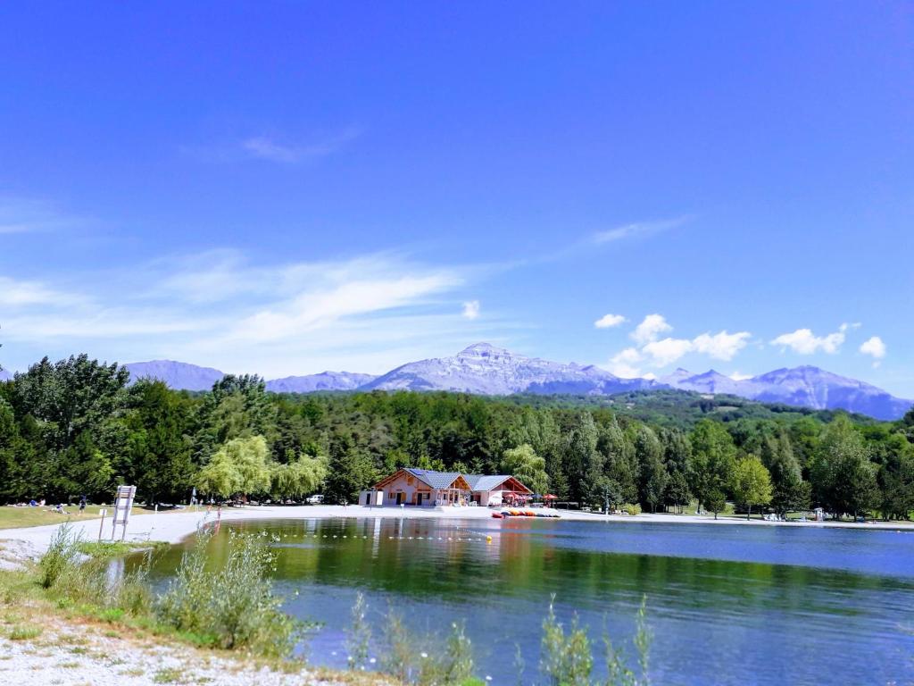 uma casa na margem de um lago com montanhas ao fundo em Petit appartement en montagne em Saint-Julien-en-Champsaur