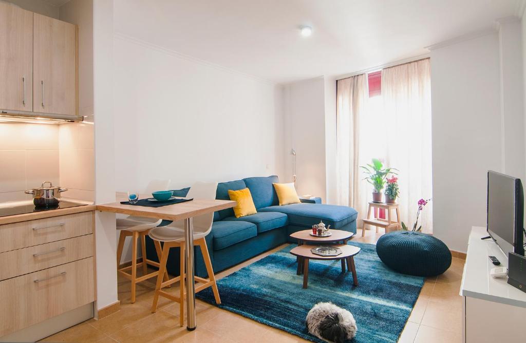 a living room with a blue couch and a kitchen at Apartamentos Vida Almería in Almería
