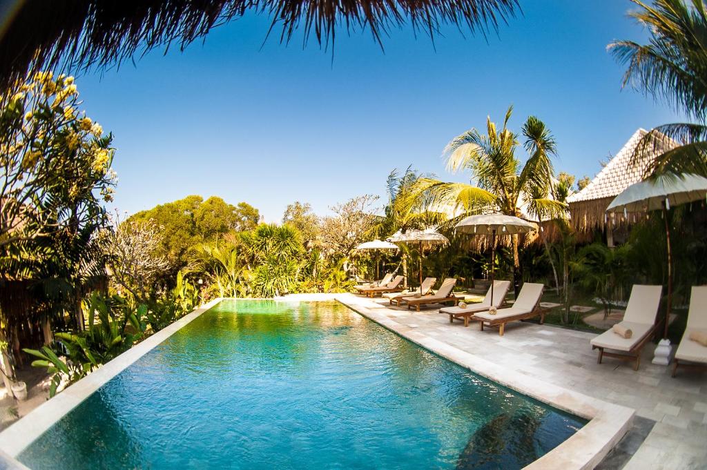 a pool with chairs and umbrellas next to a resort at Incense Impossible Beach-Adults Only in Uluwatu