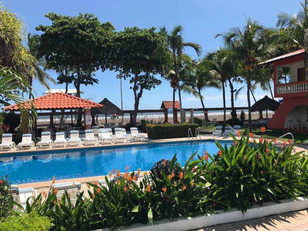 una piscina en un complejo con sillas y palmeras en Apartotel Flamboyant, en Jacó