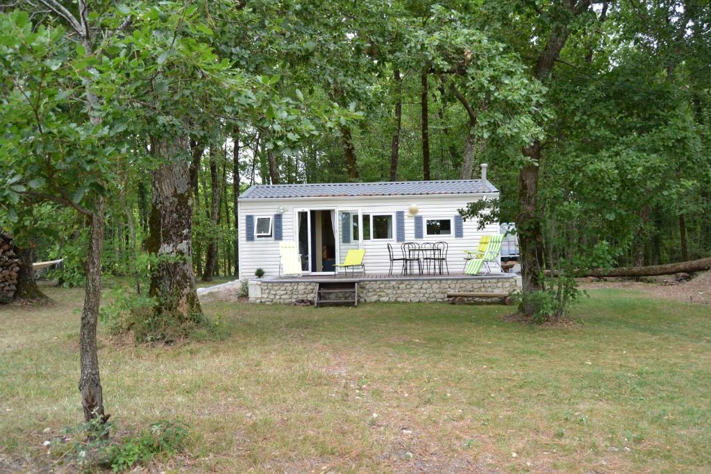 a small white cabin in the woods with trees at Mobile home des pins in Châtignac