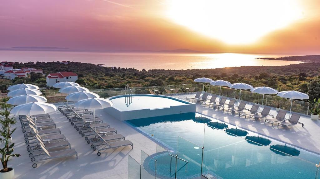 a resort with a pool and chairs and the ocean at Hotel In Excelsis in Novalja
