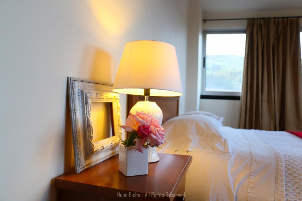 a lamp on a wooden table next to a bed at Apartamento Lombinha in Vila Franca do Campo